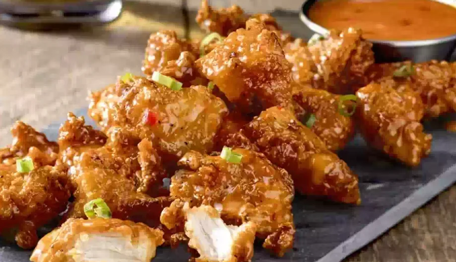 Crispy glazed chicken bites with green onion and a dipping sauce (illustrative image)