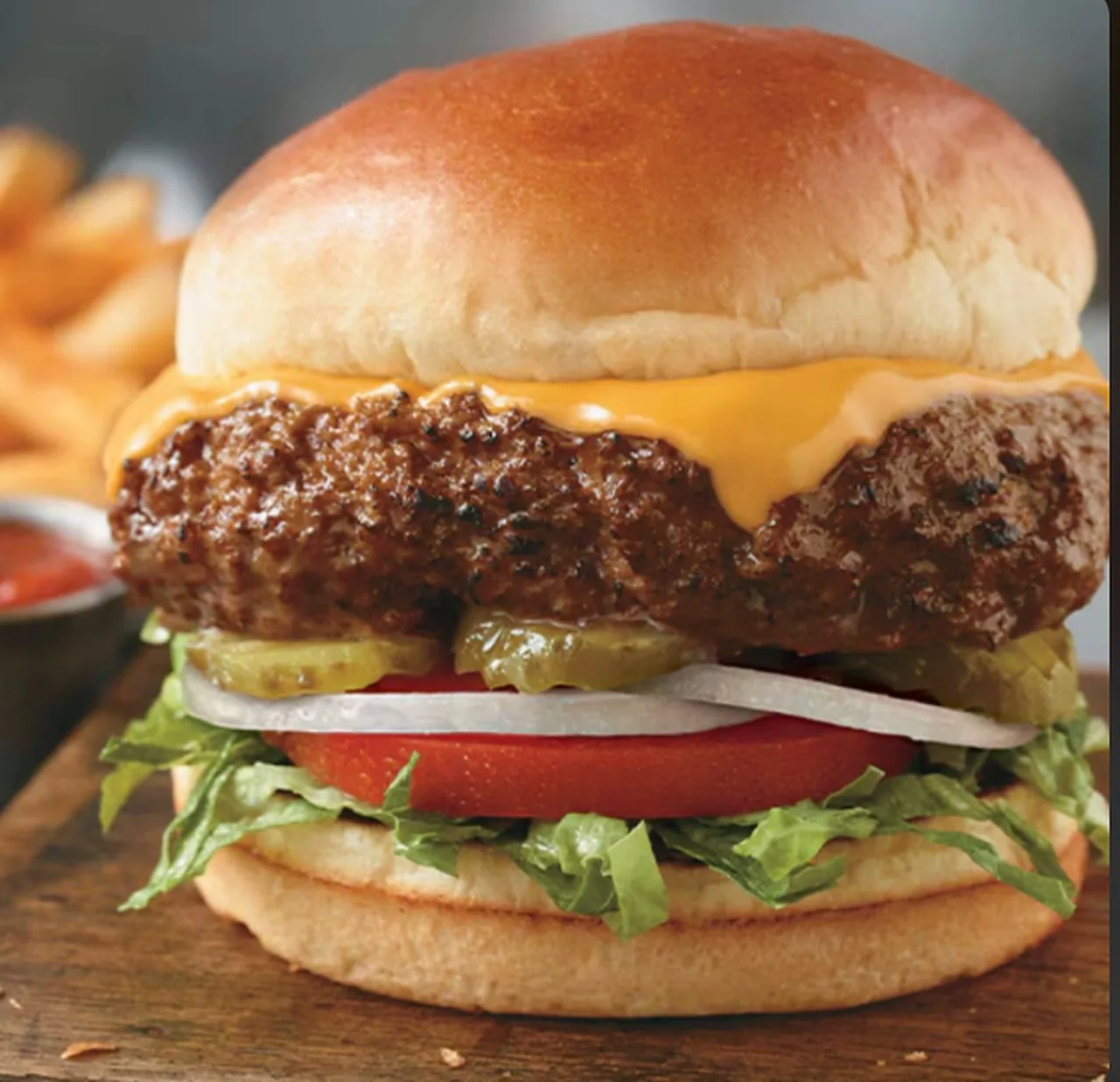 Cheeseburger with lettuce, tomato, onion and pickles, fries in the background (illustrative image)