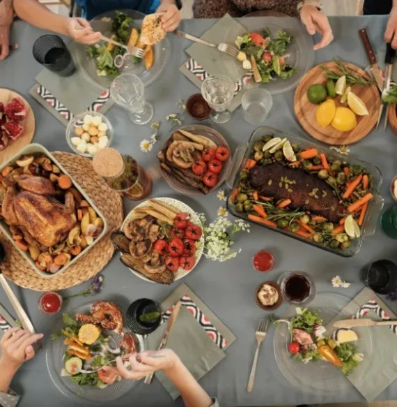 Family gathered around a table sharing roast chicken, salads and vegetables, a family meal or catering spread (illustrative image)