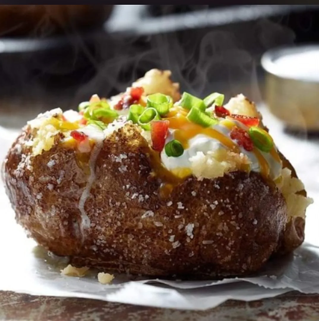 Loaded baked potato with sour cream, cheddar, bacon and green onion (illustrative image)