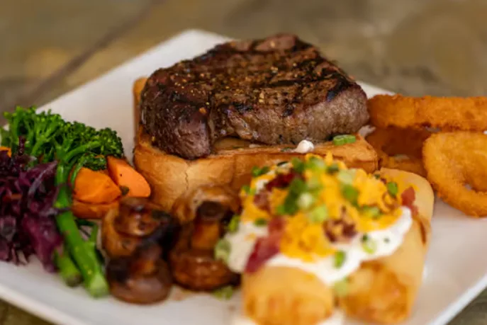 Sirloin steak on toast with loaded potato bites, vegetables and onion rings (illustrative image)